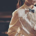 A young woman holding a flute, dressed in a white shirt and bow tie, ready to perform.