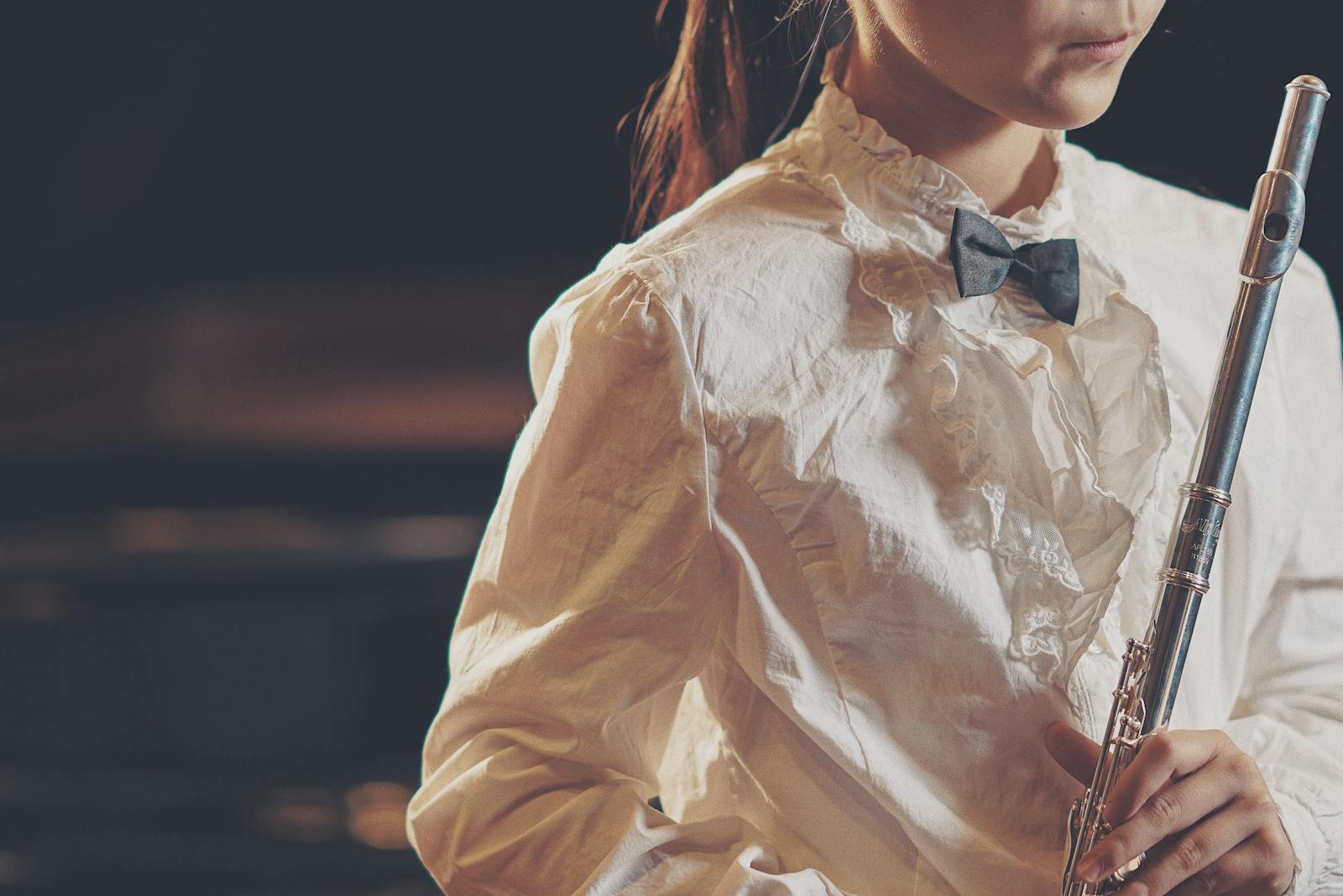 A young woman holding a flute, dressed in a white shirt and bow tie, ready to perform.