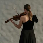 Professional female violinist in a black dress captivatingly plays indoors, focusing on her craft.