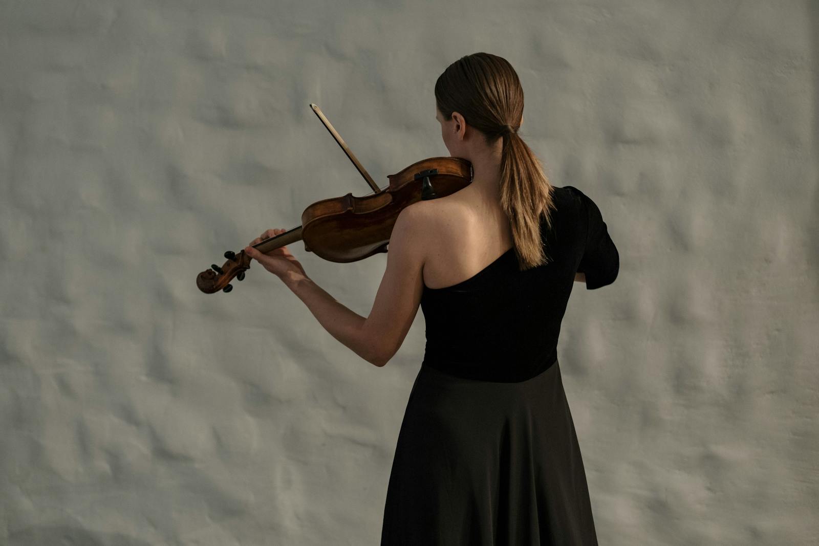 Professional female violinist in a black dress captivatingly plays indoors, focusing on her craft.