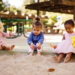 girl in pink dress sitting on brown sand during daytime